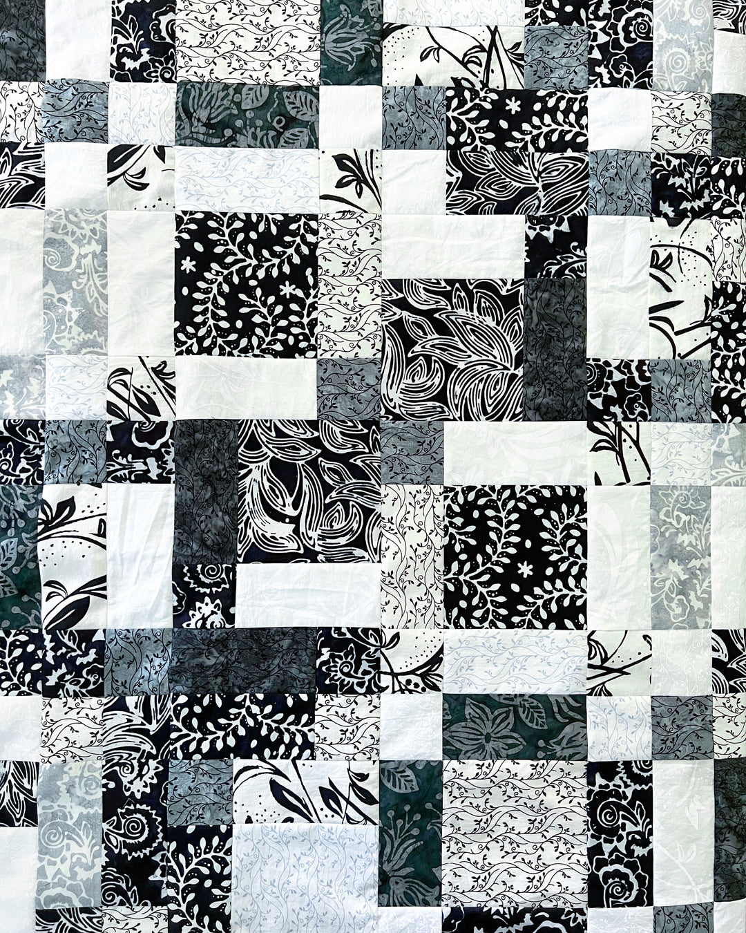 a black, gray, and white batik fabric collection called Blooms at Dusk sewn into a disappearing 16-patch quilt