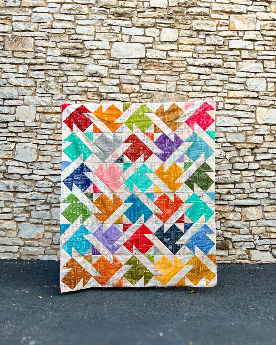 The Tactfully Twisted Quilt top made with Riley Blake Designs Typeography collection being held up in front of a limestone wall