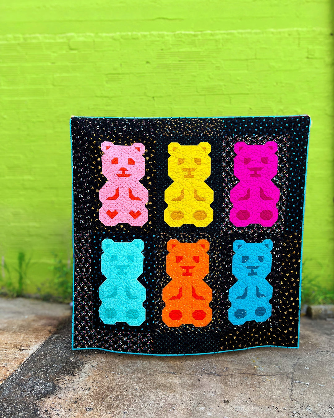 Beary Bunch Quilt Pattern with colorful bear blocks, on a black background, against a bright green wall