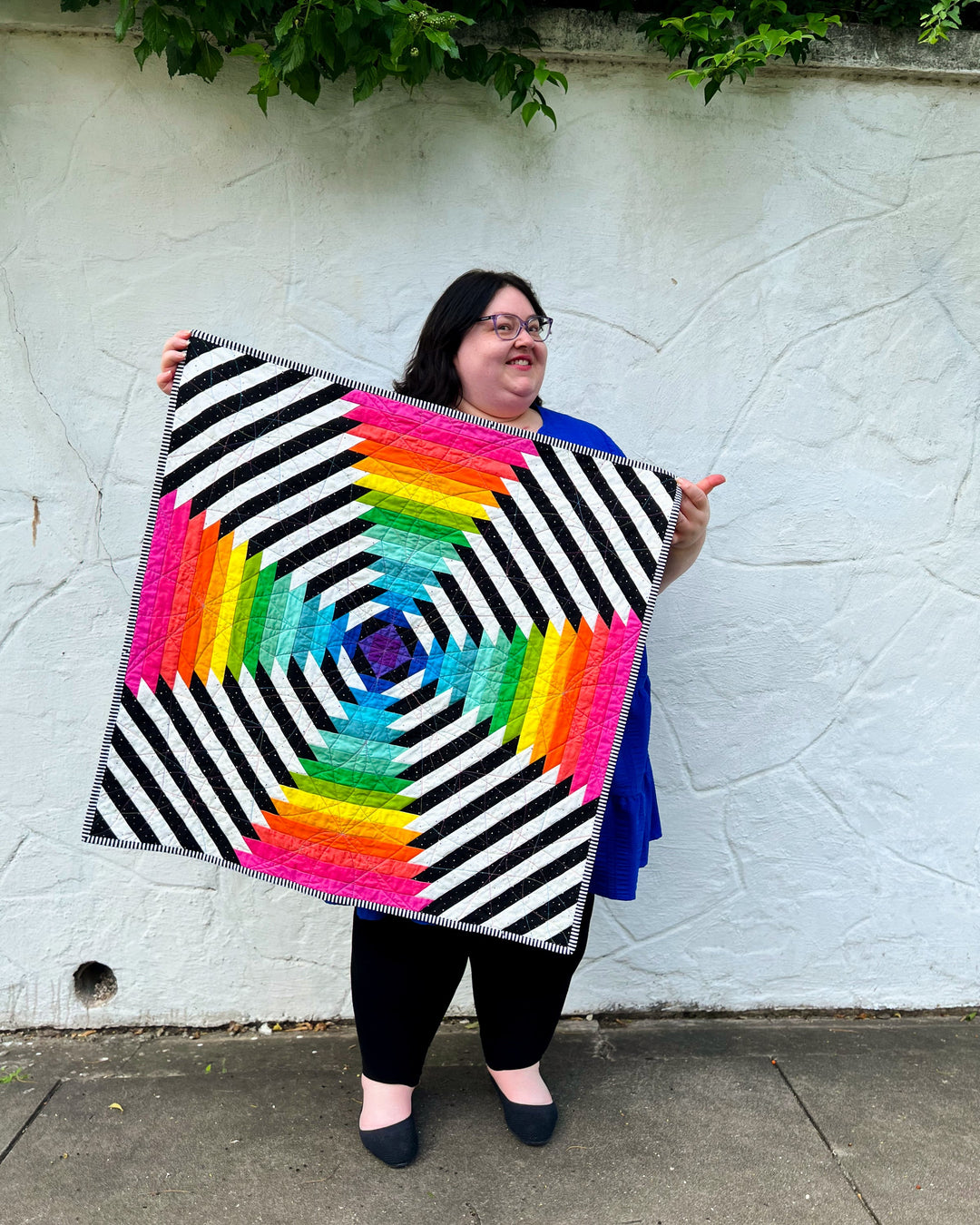 Me 'Kelly Renay' holding the Supercolossal Quilt an oversized pineapple block in front of a white textured wall