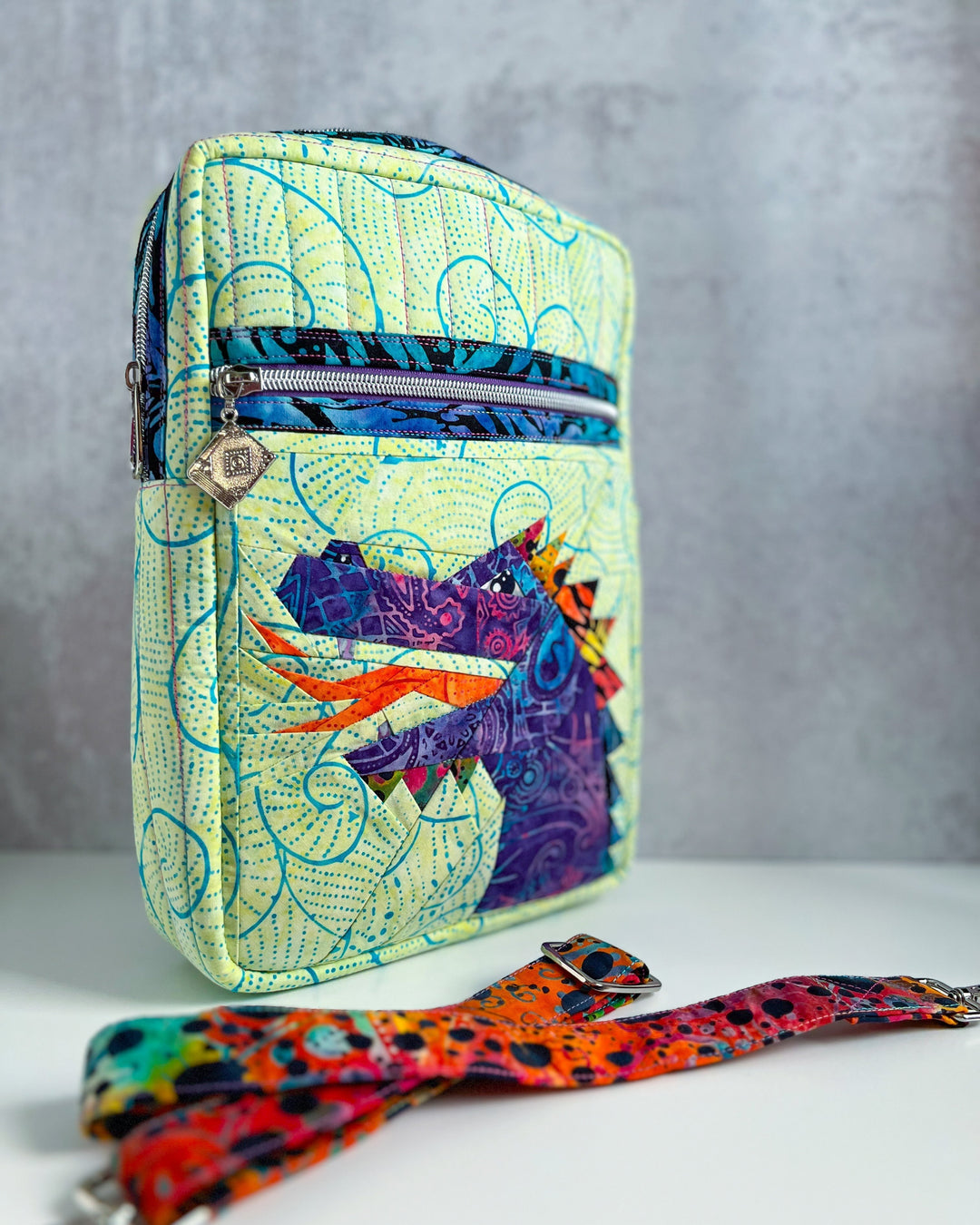 Colorful patterned crossbody bag with a purple foundation pieced dragon, and a strap on a gray background