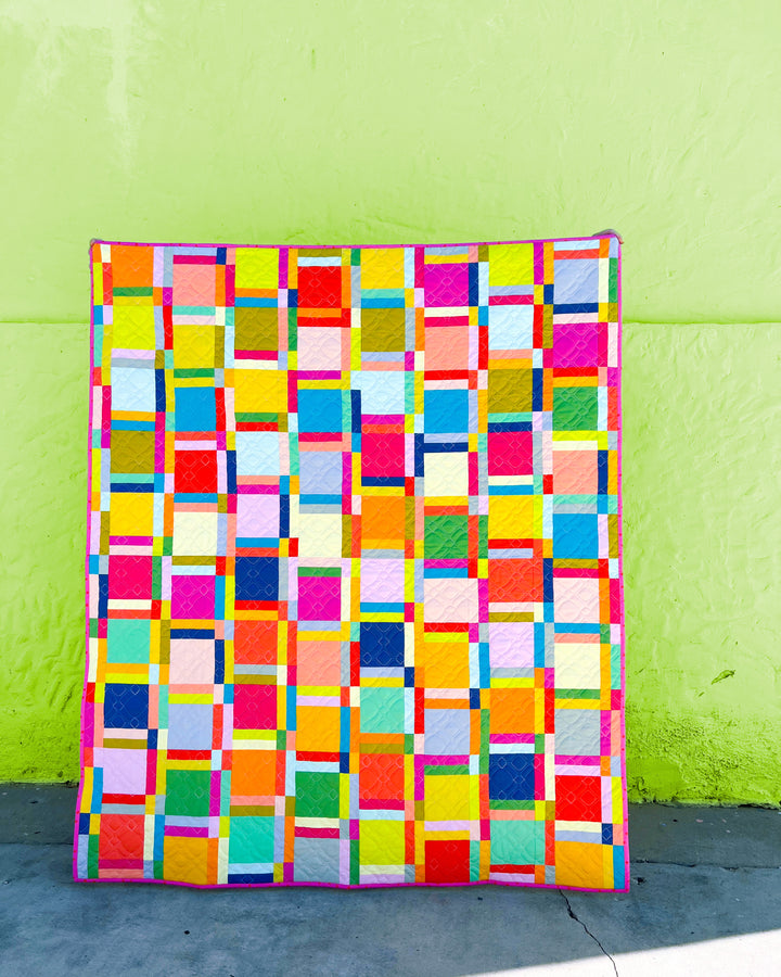 Dashing Duo quilt being held up against a green wall