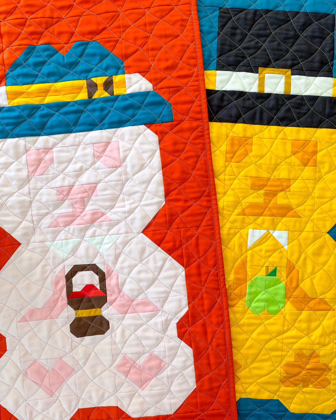 A close-up of a quilted textile featuring stylized autumn themed bear figures in bright colors, including orange, blue, white, yellow, black, green, and pink, with visible quilting stitches.