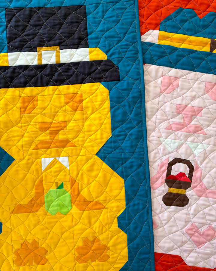 A close-up of a quilted textile featuring stylized autumn themed bear figures in bright colors, including orange, blue, white, yellow, black, green, and pink, with visible quilting stitches.