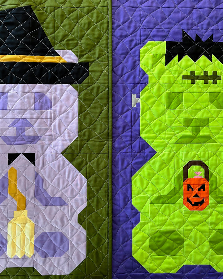 A close-up of a pair of quilts featuring two Halloween-themed bear designs: a witch in a black hat on the left over an olive green background, and a bright green monster with black hair and an orange jack-o&