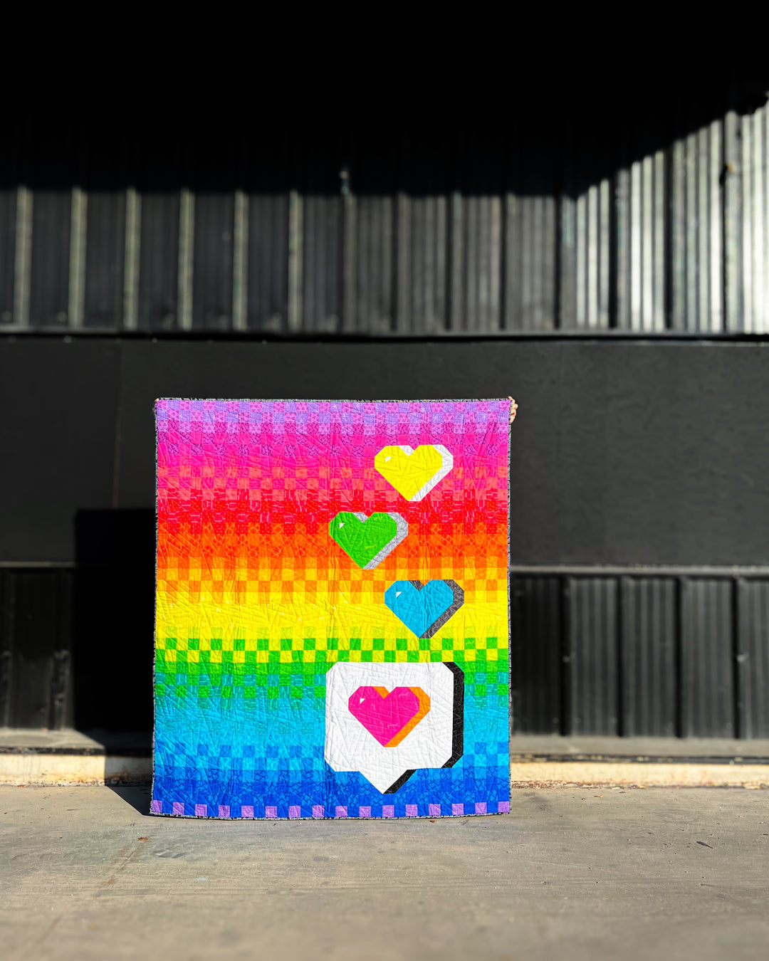 The Send with Love Quilt Pattern is a colorful pixelated art piece with heart designs on a black background