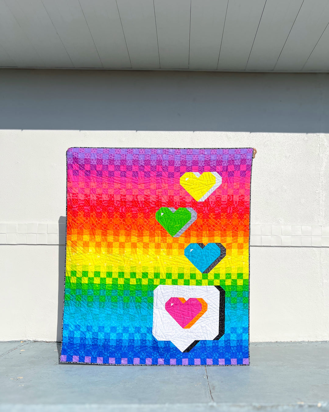 The Send with Love Quilt Pattern, a colorful quilt with heart designs on a white wall background